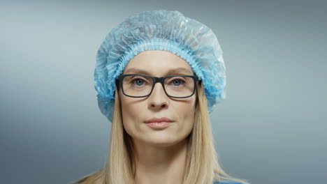 Portrait-of-the-Caucasian-beautiful-woman-physician-in-glasses,-blue-hat-smiling-joyfully-to-the-camera.-Close-up.